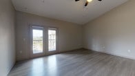 This single-floor, one-bedroom, one-bathroom unit offers a thoughtfully designed layout with a clean, modern aesthetic. Neutral-toned walls and light gray wood-style flooring run throughout the main living areas and bedroom, creating a cohesive and contemporary feel. The spacious living area benefits from vaulted ceilings and a ceiling fan, enhancing the sense of openness. French-style doors lead directly to a private balcony, flooding the space with natural light and providing outdoor views of the surrounding area.

The bedroom is generously sized, featuring the same light flooring, ample wall space, and a window that admits additional natural light. A closet door is visible, offering practical storage.

The kitchen is equipped with dark espresso cabinetry, granite-style countertops, a stainless steel refrigerator, and a single-basin sink — combining functionality with a bold contrast of finishes against the lighter flooring.

The bathroom features light tile flooring, large-format gray wall tiles surrounding a full soaking tub with a shower, a dark vanity with granite countertop, and recessed lighting, completing the unit's consistent design language.
