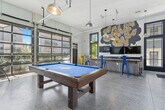 Located at 2315 South 11th Avenue in Bozeman, Montana, this single-floor game room delivers a lively, mountain-inspired atmosphere with a distinctly urban edge. The open-plan layout makes excellent use of its generous footprint, with polished concrete floors and elevated ceilings that amplify the sense of space throughout.

Floor-to-ceiling glass garage doors line one wall, flooding the interior with abundant natural light and offering views of the surrounding neighborhood. Industrial-style pendant lights hang from exposed ceiling infrastructure, reinforcing the room's modern, utilitarian aesthetic.

A central pool table with a bold blue felt surface serves as the main focal point, complemented by a rustic wood-paneled bar counter with a dark granite top and colorful metal barstools in yellow and blue. A dedicated kitchenette area features dark wood cabinetry, a granite countertop, a mounted TV, and a striking hand-lettered "Game On" mural that commands attention.

A mountain-themed art installation with a "Ski Repair" sign anchors one corner, nodding to Bozeman's outdoor recreation culture and adding a locally inspired decorative element. The space also includes additional seating along the glass doors, creating an ideal area for socializing. Overall, this game room combines playful design, functional amenities, and regional character into a cohesive and energetic communal space.