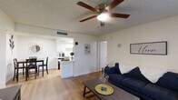 Located in Gilbert, AZ, this single-floor, 2-bedroom, 2-bathroom residence offers a well-organized layout designed for comfortable everyday living. The living room serves as the heart of the home, featuring warm wood-look flooring, a ceiling fan with light, and a window with vertical blinds that allows natural light to fill the space. The open flow connects the living area to the combined dining and kitchen space, where a compact dining nook with light-toned walls provides an intimate setting for meals. The galley-style kitchen is efficiently designed with white cabinetry, light countertops, a double-basin sink, and black appliances including a refrigerator, electric range, microwave, and dishwasher, all illuminated by a skylight-style ceiling fixture. Both bedrooms feature wood-look flooring, ceiling fans, textured ceilings, and windows with vertical blinds for light control. The primary bedroom offers a comfortable, well-proportioned layout with ample space. Both bathrooms are clean and functional, each equipped with a tub-shower combination featuring a curved curtain rod and chrome fixtures. Three closets throughout the unit provide convenient storage solutions. The overall ambiance is bright, neutral, and move-in ready.