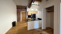Located at 423 N 18th St in Richmond, VA, this one-bedroom, one-bathroom unit blends historic character with modern updates. The open living area flows seamlessly into the kitchen, which features a peninsula with dark granite countertops, light wood cabinetry, stainless steel appliances including a range and refrigerator, and pendant lighting suspended from striking exposed wood beams overhead. Warm hardwood floors run throughout, complementing the unit's industrial-chic aesthetic.

A defining feature of the space is the exposed brick wall, visible from both the main living area and the bedroom, lending authentic historic charm. The bedroom is generously proportioned, with soaring ceilings accented by wood beams, a ceiling fan, and a window set into the brick wall that brings in natural light and outdoor views. The clean white walls provide a neutral contrast to the rich textures of brick and wood throughout.

The bathroom is clean and functional, offering a combined tub and shower with chrome fixtures and tile flooring. Throughout the unit, thoughtful design details — from the barn-style door to the high ceilings — create an ambiance that is both cozy and characterful, making this a distinctive offering in Richmond's historic landscape.