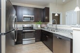 This single-story residence at 700 SR-96 E in Bonaire, Georgia, offers a thoughtfully designed layout with a cohesive, neutral aesthetic throughout. The open-concept kitchen serves as a functional centerpiece, featuring rich dark cabinetry, granite countertops, stainless steel appliances, and a breakfast bar illuminated by pendant lighting. Light wood-style flooring runs through the kitchen and connects seamlessly to the surrounding living areas.

The living room is a comfortable, well-lit space with a ceiling fan, large windows dressed in floor-length drapes, and warm, neutral tones that create a relaxed atmosphere. Multiple bedrooms provide versatile accommodations, each equipped with ceiling fans, natural light from windows with blinds and curtain panels, and wood-style flooring. The bedrooms maintain a calm, restful ambiance with ample closet space.

The bathrooms continue the granite countertop theme, with dark vanity cabinetry complementing the overall design palette. One bathroom features a tub-shower combination, while another offers additional utility space with built-in shelving. The consistent use of neutral tones, quality finishes, and natural light throughout the home creates a polished and inviting environment.