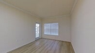 This single-story, 1-bedroom, 1-bathroom unit offers a practical and comfortable layout across a compact but efficient floor plan. The open-concept living area greets you upon entry, featuring light wood-look flooring, crown molding, and a large window fitted with blinds that allows natural light to fill the space. A pass-through kitchen sits adjacent to the living area, outfitted with white cabinetry, a microwave, and a refrigerator, all accented by under-cabinet lighting for a clean, functional aesthetic. The bedroom is a cozy retreat, finished with plush carpet, a ceiling fan with light fixture, and a window with blinds for controlled natural light. A spacious walk-in closet off the bedroom provides ample storage with wire shelving systems. The full bathroom includes a single-sink vanity with white cabinetry, a tiled tub-shower combination, and tile flooring, creating a clean and practical space. A dedicated laundry area houses a top-load washer and includes overhead shelving. Neutral, warm-toned walls throughout lend a cohesive and inviting atmosphere to this well-organized unit.