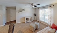 This single-floor residence presents a thoughtfully designed layout that balances functionality with comfort. The kitchen is equipped with dark espresso cabinetry, granite countertops, and a full suite of stainless steel appliances, including a range, built-in microwave, dishwasher, and refrigerator. Wood-look flooring grounds the space, complementing the rich cabinetry tones.

The bedroom is generously proportioned, featuring plush wall-to-wall carpeting and a ceiling fan for year-round comfort. Vertical blinds cover a sliding glass door that provides direct outdoor access and brings in natural light. The room offers ample space for a full furniture arrangement, including a dresser and seating area.

The living area is carpeted and bright, with a ceiling fan overhead and a window that frames outdoor views. Neutral wall tones throughout the residence create a cohesive, understated aesthetic. The floor plan, as indicated by the overhead model, flows openly between the main living spaces, kitchen, and bedroom, making efficient use of the available footprint while maintaining a welcoming atmosphere.