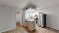 Located at 2712 W Tharpe St in Tallahassee, Florida, this single-floor residence offers a clean, updated interior with a cohesive design aesthetic throughout. Light-toned wood-look flooring flows seamlessly across all living areas, complementing the neutral gray and white color palette that gives the space a fresh, modern feel.

The kitchen is a standout feature, equipped with white shaker-style cabinetry, granite-look countertops, and a full suite of stainless steel appliances including a refrigerator, range, and over-the-range microwave. A peninsula with built-in shelving provides additional storage and casual seating, while pendant lighting overhead adds a polished touch. The kitchen opens toward the main living area, creating an efficient and connected layout.

The living area is open and well-lit, with access to the front entry door and a clear sightline into the kitchen. The bedrooms are comfortably sized, each featuring natural light from windows overlooking the surrounding greenery, ceiling fans for climate comfort, and the same consistent flooring found throughout the home.

The bathroom is neatly appointed with a white vanity, granite-look countertop, framed mirror, and light fixture, maintaining the clean and updated style of the rest of the space. Overall, this residence presents a well-maintained, move-in-ready interior with practical features and a cohesive modern design.