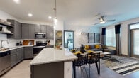 This thoughtfully designed single-floor residence offers a seamless open-concept layout that connects the kitchen, dining, and living areas into one cohesive, light-filled space. The kitchen is a standout feature, showcasing gray shaker-style cabinetry, stainless steel appliances including a French door refrigerator, built-in microwave, and dishwasher, as well as a granite-topped island with bar seating. A white subway tile backsplash and light wood-look flooring complete the kitchen's clean, modern aesthetic. Pendant lighting over the island and recessed ceiling lights enhance the open ambiance.

The dining area flows naturally from the kitchen, while the living room offers generous space highlighted by a ceiling fan and a gallery wall of bold abstract artwork. Natural light pours in through multiple windows dressed with sleek blinds and dark accent curtains.

The primary bedroom is a serene retreat with plush carpet, multiple windows, a ceiling fan, and ample natural light. Its en-suite bathroom features granite countertops, gray cabinetry, a glass-enclosed walk-in shower, and access to a walk-in closet. The second bedroom mirrors the same comfort with carpet flooring, a ceiling fan, and a bold two-tone accent wall. A second full bathroom with granite countertops and a tub-shower combination serves this bedroom, maintaining the residence's consistent, modern design language throughout.