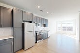 Located at 9420 Grand Blvd in Upper Marlboro, MD, this single-floor, three-bedroom, one-bathroom residence offers a well-designed layout with modern finishes throughout. The open-concept living, dining, and kitchen area serves as the heart of the home, featuring soaring ceilings that enhance the sense of space. Large windows flood the living area with natural light and offer views of the surrounding greenery. The kitchen is outfitted with gray shaker-style cabinetry, quartz countertops, a white subway tile backsplash, and a full suite of stainless steel appliances including a refrigerator, range, microwave, and dishwasher. Light wood-tone flooring flows consistently throughout the home. A central hallway connects the three bedrooms, an office, and the full bathroom. The primary bedroom benefits from generous natural light through large windows with outdoor views. The bathroom features a subway-tiled tub-shower combo, a quartz-topped vanity with a gray cabinet, and wood-tone flooring. Four closets, including walk-in style storage with wire shelving, provide ample organization. A dedicated laundry area adds everyday convenience to this thoughtfully planned residence.