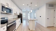 Located at 3014 Dr. Martin Luther King Jr. St. S in Saint Petersburg, FL, this well-designed one-bedroom, one-bathroom unit offers a thoughtfully organized single-floor layout. Light hardwood-style flooring flows seamlessly throughout the entire space, creating a cohesive and clean aesthetic.

The open-concept kitchen serves as a central highlight, featuring white shaker cabinetry with matte black hardware, granite countertops, and a full suite of stainless steel appliances including a refrigerator, range, microwave, and dishwasher. A kitchen island with matching granite provides additional prep space and anchors the connection between the kitchen and living area. Stylish pendant lights hang overhead, complemented by recessed ceiling lighting. A ceiling fan adds comfort to the living area, which receives natural light through multiple windows.

The bedroom is a bright and calm retreat, benefiting from natural light through slatted blinds. Two closets provide ample storage. The hallway connects the living spaces to the bathroom, which features light cabinetry with black hardware consistent with the overall design language. A washer is also visible within the unit, adding convenience. The clean, neutral palette and modern finishes throughout make this a move-in ready space.