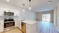 Located at 20–26 Everett Rd Ext in Albany, NY, this one-bedroom, one-bathroom unit offers a thoughtfully designed open-concept layout with contemporary finishes throughout. Light-toned hardwood flooring runs through the main living areas, creating a cohesive and bright aesthetic that complements the neutral wall palette.

The kitchen and living room share an open, connected space centered around a peninsula with a white quartz countertop, undermount sink, and stainless steel appliances, including a range, microwave, and dishwasher. White shaker cabinetry and a subway tile backsplash add clean, modern detailing, while two glass pendant lights suspended above the peninsula serve as a focal point. A sliding glass door in the living area provides access to a private balcony and allows natural light to fill the room.

The bedroom is comfortably sized, finished with plush carpeting, and features a window with outdoor views. The bathroom includes a full walk-in shower with a built-in bench. A dedicated laundry area accommodates a full-sized washer and dryer, adding practical convenience to the unit's overall well-appointed design.