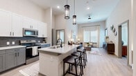 This thoughtfully designed 2-bedroom, 3-bathroom single-story residence offers a seamless open-concept layout that connects the kitchen, dining, and living areas into one cohesive living space. Soaring ceilings amplify the sense of openness, while large windows flood the interior with abundant natural light throughout the day.

The gourmet kitchen is a standout feature, showcasing two-tone cabinetry with crisp white upper cabinets and slate-gray lowers, a dark subway tile backsplash, stainless steel appliances, and a spacious quartz-topped island with bar seating and elegant pendant lighting overhead. The adjoining living room continues the airy feel with its dramatic ceiling height and generous window treatments.

Light wood-tone flooring flows consistently throughout the unit, complementing the neutral, warm color palette. The primary bedroom is a comfortable retreat with bright windows, wood-look floors, and access to a dedicated bathroom featuring a quartz vanity, gray cabinetry with matte black hardware, and a tiled walk-in shower. Two well-appointed closets provide ample storage, including a spacious walk-in with built-in shelving and hanging rods. Each of the three bathrooms reflects the same refined, modern aesthetic found throughout the home.