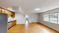 This single-floor unit offers a consistent and functional layout highlighted by warm-toned hardwood flooring that runs throughout every room, creating a cohesive and inviting atmosphere. The neutral light-gray walls and white trim provide a clean, versatile backdrop, while textured ceilings add a classic architectural detail.

The kitchen is well-equipped with a full suite of stainless steel appliances, including a refrigerator, range, microwave, and dishwasher. Warm wood cabinetry lines the walls both above and below the countertops, offering generous storage, and a single-basin sink is conveniently positioned beneath upper cabinets. The kitchen opens naturally toward the main living area, which is spacious and bright, with windows allowing natural light and views of surrounding greenery.

Multiple additional rooms are present throughout the unit, each featuring hardwood floors, windows with blinds, and closets equipped with built-in shelving and hanging rods—providing practical storage solutions. The bathroom includes a full tub-shower combination with a crisp white surround and integrated corner shelving. A hallway connects the rooms, maintaining a clear and organized flow throughout the space. Ceiling-mounted flush lighting and HVAC vents are present throughout.