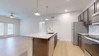 This single-story residence offers 2 bedrooms and 3 bathrooms within a thoughtfully designed open-concept layout. Light-toned hardwood flooring runs throughout, lending a clean, cohesive aesthetic to every room.

The kitchen serves as a central focal point, anchored by a large island with a granite countertop, undermount double sink, and pendant lighting overhead. Dark espresso cabinetry contrasts with the light stone surfaces, while a full suite of stainless steel appliances—including a refrigerator, range, microwave, and dishwasher—completes the space.

The living room is bright and open, featuring vaulted ceilings, a ceiling fan, and French doors that allow natural light to fill the room and provide outdoor access. The neutral wall tones enhance the airy atmosphere.

The primary bedroom offers a comfortable footprint with access to a walk-in closet fitted with wire shelving systems for organized storage. The bathrooms maintain the same design language as the rest of the unit, with granite-topped dark wood vanities, undermount sinks, and a tub-shower combination finished in clean white tile. Two hallways and additional closets provide practical storage and circulation throughout the residence.