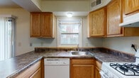 Located at 440 Alexandria Colony Ct W in Columbus, Ohio, this two-story residence offers a straightforward, functional layout distributed across two levels. The main floor features hard surface flooring at the entryway, transitioning to carpet in the spacious living area. A staircase with a metal railing connects the two floors, providing an open sightline from the entry. The kitchen is equipped with warm oak cabinetry, dark laminate countertops, a stainless steel sink, a white dishwasher, and a white range, with a window above the sink allowing natural light and views of the surrounding exterior. A full bathroom on the main level features white square tile surroundings on the tub/shower combination, textured walls, and wood-look flooring. The upper level hosts carpeted bedrooms, including one with a double-door closet offering built-in shelving and hanging space, and another room with a window providing natural light. A second full bathroom upstairs features an oak vanity with a white countertop, a tiled tub/shower, textured walls, and wood-look flooring, complemented by chrome fixtures throughout.