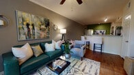 This well-appointed single-floor residence offers a thoughtfully designed open-concept layout that seamlessly connects the living, dining, and kitchen areas. The living room makes a strong first impression with warm hardwood flooring, crown molding, and a ceiling fan overhead. A rich teal sofa anchors the space, complemented by a geometric area rug, wall sconces, and a vibrant abstract painting that adds a splash of color against the taupe-toned walls.

The kitchen is a functional and attractive space, featuring white shaker-style cabinetry, granite countertops, a tile backsplash, and a full suite of stainless steel appliances including a refrigerator, range, and microwave. A breakfast bar with tall seating connects the kitchen to the main living area, while an arched architectural detail adds a classic touch.

The bedroom is bright and serene, with warm yellow accent walls, plush carpeting, and a generously sized window that draws in natural light. A walk-in closet provides ample storage, enhancing the room's practicality.

The bathroom is clean and well-finished, showcasing granite countertops, white cabinetry with brushed nickel hardware, rich hardwood-style flooring, and a full tub-shower combination. Throughout the space, consistent finishes and warm tones create a cohesive and inviting atmosphere.