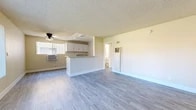 Located at 132 S Westchester Dr in Anaheim, California, this 2-bedroom, 1-bathroom single-floor unit offers a practical and well-maintained layout. The combined living room and kitchen area forms the heart of the home, featuring durable wood-look luxury vinyl flooring, a textured ceiling, and a ceiling fan. The kitchen is equipped with white cabinetry, granite-style countertops, a double-basin sink, and a peninsula that provides additional counter space and defines the transition between cooking and living areas. A large window with vertical blinds fills the living area with natural light and offers a view of the surrounding greenery. Both bedrooms are carpeted and feature ceiling fans, neutral warm walls, and windows dressed with vertical blinds that allow ample daylight. The primary bedroom is generously proportioned and includes closet access. The second bedroom is equally well-lit and versatile. The full bathroom is clean and bright, finished with wood-look flooring, a white vanity, a tub-shower combination, and a window for ventilation. A connecting hallway and two closets provide convenient storage throughout the unit. Wall-mounted air conditioning units offer dedicated climate control.