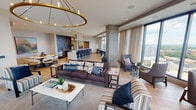 Located at 1007 Church St in Evanston, Illinois, this elevated single-floor space delivers a refined, contemporary design with an open, flowing layout. Light oak hardwood flooring extends throughout, unifying the various functional zones beneath crisp white ceilings with recessed lighting.

The expansive lounge area serves as the centerpiece, anchored by a statement circular brass chandelier and a wall-mounted display above a sleek fireplace. Multiple seating arrangements — including plush sofas, accent chairs, and side tables — offer flexible social configurations. Exposed concrete columns add an industrial counterpoint to the otherwise polished interior.

Floor-to-ceiling windows wrap around the perimeter, flooding the space with natural light and framing panoramic views of the Evanston skyline and Lake Michigan beyond. Sheer linen drapery softens the glass line while preserving the visual connection to the outdoors.

A fully equipped kitchen and bar area features dark cabinetry, stainless steel appliances, a textured metallic backsplash, and bar seating, making it well-suited for catered events or casual gatherings. An adjacent dining nook showcases a round marble-topped table paired with upholstered chairs and a colorful landscape painting.

Curated artwork displayed throughout the space adds warmth and personality, complementing the neutral, modern palette and creating an inviting, gallery-like atmosphere.