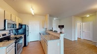 Located at 104 S Kirkwood Rd in Kirkwood, Missouri, this single-floor unit offers a thoughtfully designed open-concept layout that seamlessly connects the kitchen and living areas. The kitchen is a standout feature, with a galley-style configuration equipped with stainless steel appliances, including a refrigerator, range, and built-in microwave. Light-toned cabinetry provides ample storage, while granite-style countertops extend to a peninsula that doubles as a casual dining or serving area, creating a natural boundary between the kitchen and the living space. Track lighting illuminates the kitchen efficiently.

The living area is finished with warm hardwood-style flooring and features crown molding that adds a polished architectural detail. A door leads to an outdoor area, allowing natural light to filter into the space. Neutral wall tones throughout create a versatile, welcoming ambiance.

The bedroom is carpeted and benefits from a large window that brings in generous natural light. The bathroom includes a vanity with a sink and a shower enclosed by a curtain. A hallway connects the main living areas to the private spaces, with louvered closet doors providing practical storage solutions. Overall, the unit presents a clean, functional, and comfortable living environment.