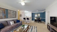 Located at 1160 Auston Grove Rd in Raleigh, NC, this single-floor residence offers a well-designed layout that balances comfort and functionality. The open-concept living and dining area serves as the heart of the home, finished with plush carpeting, crown molding, and a ceiling fan overhead. The living room provides generous space for relaxing, while the adjacent dining area is distinguished by rich, deep-blue accent walls, chair rail molding, and mirrored wall décor that adds depth and elegance. The galley-style kitchen features white cabinetry, wood-look flooring, a full suite of white appliances, and a breakfast bar with bar seating — ideal for casual dining. The bedrooms are comfortably sized with soft carpet underfoot; the secondary bedroom benefits from a tall window that invites natural light and views of surrounding greenery. Two full bathrooms serve the home — one with a shower and one with a shower-tub combination — both finished with wood-look flooring, white vanity cabinetry, and clean, neutral tones. A dedicated in-unit laundry area with a full-size washer adds everyday convenience. Throughout the space, a cohesive neutral palette punctuated by bold blue accents creates a warm and inviting ambiance.