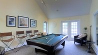 Located at 5450 Firewater Ln in Westerville, Ohio, this single-floor community amenity space is designed to offer residents a welcoming and recreational environment. The standout feature of the space is a well-appointed game room centered around a full-size pool table with a rich green felt surface, providing a focal point for leisure and social interaction. The room is elevated by dramatic vaulted ceilings that amplify the sense of openness and airiness throughout. Warm, light-toned walls complement the neutral carpeted flooring, creating a clean and inviting atmosphere. Seating is provided along the perimeter, offering comfortable spots for onlookers and guests. Natural light floods the space through multiple sets of French doors and large windows, connecting the interior to the lush greenery visible outside. Track lighting along the ceiling ensures the room remains well-lit at all times. Decorative framed artwork adorns the walls, adding a polished, curated aesthetic to the recreational setting. The French doors provide convenient access to the outdoor surroundings, seamlessly blending indoor comfort with outdoor accessibility. Overall, this amenity space combines functional design with an inviting ambiance, making it an ideal gathering spot for recreation and community engagement.