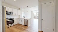 Located at 141 Danbury Rd in Wilton, CT, this contemporary two-bedroom, two-bathroom residence spans two floors and delivers a bright, modern aesthetic throughout. The main floor centers on an open-concept kitchen and living area flooded with natural light from oversized floor-to-ceiling windows and sliding glass doors that open to a private balcony overlooking the surrounding community. The kitchen is thoughtfully designed with crisp white shaker cabinetry, subway tile backsplash, stainless steel appliances including a gas range, dishwasher, and refrigerator, and sleek pendant lighting over the peninsula. Light hardwood flooring flows seamlessly through the kitchen and living spaces, enhancing the airy, open feel. Both bedrooms offer plush wall-to-wall carpeting and generous windows that bring in natural light. The primary bedroom includes access to a dedicated closet. The two bathrooms are finished with clean white tile, modern vanities, and illuminated mirrors — one featuring a walk-in glass shower, the other a full soaking tub and shower combination. A standout feature of this residence is the expansive private rooftop terrace, finished with large-format pavers and protected by sleek metal railings, offering sweeping open-sky views — an ideal outdoor retreat.