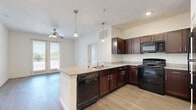 This single-story, two-bedroom, two-bathroom unit in Austin, Texas offers a well-organized layout with wood-style flooring throughout the main living areas and plush carpet in the bedrooms. The open-concept kitchen serves as a central hub, featuring rich dark-wood cabinetry, granite countertops, a peninsula island with an integrated sink and dishwasher, pendant lighting, and black appliances including a gas range, microwave, and refrigerator. The kitchen flows directly into the living area, which is brightened by a ceiling fan and French doors opening to a private balcony with outdoor views.

Both bedrooms are carpeted and include ceiling fans and windows with blinds that invite natural light. Each bedroom is served by its own dedicated bathroom and walk-in closet. The walk-in closets are outfitted with wire shelving systems, providing organized storage. The bathrooms feature wood-style flooring, dark-wood vanities with white countertops, large mirrors, and updated light fixtures.

A connecting hallway links the bedrooms and bathrooms to the main living spaces, creating a functional and efficient floor plan. The unit's neutral color palette and consistent finishes throughout contribute to a cohesive, move-in-ready ambiance.