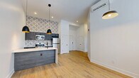 This thoughtfully designed one-bedroom, one-bathroom unit at 2801 S Pennsylvania St in Indianapolis offers a clean, modern aesthetic with high-quality finishes throughout. Light wood-tone flooring runs continuously across the open layout, complementing the crisp white walls and creating a bright, airy atmosphere. The kitchen is a standout feature, anchored by a peninsula with a striking marble-look quartz countertop, an undermount sink with a matte black faucet, and dark wood-tone cabinetry. A bold geometric-patterned tile backsplash adds visual interest, while stainless steel appliances — including a refrigerator, range, microwave, and dishwasher — complete the space. Stylish black pendant lights with gold interiors illuminate both the kitchen and dining area. The spacious bedroom features a wall of windows that floods the room with natural light and offers outdoor views, along with a dedicated closet with built-in shelving and a wall-mounted mini-split HVAC unit. The bathroom is finished with large hexagonal marble-look floor tiles, a soaking tub with a curved rod, dark-toned vanity cabinetry, and a white quartz countertop, delivering a polished and cohesive design.