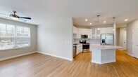 Located at 4555 McCrimmon Pkwy in Morrisville, NC, this single-floor residence offers a clean, modern aesthetic with thoughtfully designed living spaces. The open-concept layout connects the living area and kitchen seamlessly, with warm light hardwood flooring extending throughout the main living areas. Large windows with blinds allow generous natural light to fill the space, and a ceiling fan keeps the living room comfortable year-round. A sliding glass door provides access to an outdoor balcony area.

The kitchen is well-appointed with crisp white cabinetry — including glass-front upper cabinets — a subway tile backsplash, light quartz countertops, and a full suite of stainless steel appliances including a refrigerator with ice maker, electric range, built-in microwave, and dishwasher. A kitchen island adds additional prep and dining space.

The bedrooms feature plush carpeting, ceiling fans, and closets with built-in wire shelving systems. Bathrooms are finished with light hardwood-style flooring, white dual-sink vanities with quartz countertops, and marble-look tile. One bathroom offers a glass-enclosed walk-in shower, while another features a soaking tub with brushed gold fixtures and full marble-tile surround.