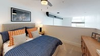 Located at 3560 E La Palma Ave in Anaheim, CA, this two-story loft offers a striking blend of industrial and contemporary design. The main level welcomes you with soaring double-height ceilings and expansive floor-to-ceiling windows flanking glass French doors, flooding the space with natural light and providing views of the surrounding area. Light wood-toned flooring runs throughout, anchoring the open-plan living area, which features a curated gallery wall, warm-toned furnishings, and bold accent pieces that lend a modern, artistic character. The kitchen is thoughtfully designed with flat-front natural wood cabinetry, white quartz countertops, a geometric tile backsplash, stainless steel appliances, and a central island with seating — ideal for both cooking and entertaining. Two bathrooms echo the same design sensibility, featuring warm wood vanities, white countertops, round black-framed mirrors, and wood-look tile flooring. A staircase leads to the upper level, where the bedroom retreat offers carpeted flooring, a ceiling fan, and an open overlook connecting it to the dramatic main living volume below. An additional bedroom on the upper level provides soft carpeting, ample closet access, and a calm, restful atmosphere. This loft delivers a compelling combination of scale, style, and functionality.