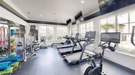 The Kendall Fitness Center at 1101 Flagstone Lane in Indian Trail, NC is a thoughtfully designed community gym space that offers a comprehensive workout experience. The interior features a clean, modern aesthetic with white walls accented by a bold dark horizontal band near the crown molding, lending the space a polished, purposeful character. Recessed lighting and large, multi-pane windows along multiple walls flood the room with natural light while offering views of the surrounding community.

The fitness floor is outfitted with durable dark rubber flooring and a wide array of equipment to support varied workout routines. Cardio offerings include multiple treadmills, stationary bikes — including a Peloton-style cycle — an elliptical, and an Echelon rowing machine. A cable and pulley strength system anchors the strength training area, complemented by a full dumbbell rack and various resistance machines, including a leg press. Colorful stability and exercise balls add a functional flexibility and core training option.

Wall-mounted flat-screen televisions are positioned throughout for entertainment during workouts. A water cooler provides convenient hydration access. French-style glass doors connect to an adjacent area, and large mirrors enhance the sense of openness. Fitness center rules and signage from The Kendall community are prominently displayed, reinforcing a well-managed, community-oriented environment.