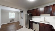 This single-floor residence at Jumping Brook, Building 12, Unit 267, offers a well-designed layout with a neutral color palette and dark hardwood flooring throughout the main living areas. The kitchen is outfitted with rich dark-wood cabinetry, white countertops, stainless steel appliances including a refrigerator, dishwasher, and electric range, as well as a stainless steel sink. A stacked in-unit washer and dryer is conveniently located adjacent to the kitchen, which opens directly into the dining area, illuminated by a pendant light fixture and a window overlooking greenery.

The living room is generously proportioned, featuring a sliding glass door with vertical blinds that allows natural light to fill the space and provides access to an outdoor area. Baseboard heating is present throughout. The bedrooms continue the hardwood flooring theme and are well-lit by exterior-facing windows. One bedroom features dual closets, offering ample storage. The bathroom is cleanly finished with white tile surrounding a full soaking tub and shower, gray tile flooring, and modern chrome fixtures. Overall, the unit presents a clean, functional, and comfortable living environment.