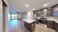 Located at 212 Locust St in Monticello, MN, this 2-bedroom, 2-bathroom residence offers a well-designed open-concept layout with modern finishes throughout. The kitchen is a standout feature, equipped with rich dark-espresso cabinetry, granite-look countertops, a central island, and a full suite of stainless steel appliances including a refrigerator, range, microwave, and dishwasher. Wood-look luxury vinyl plank flooring flows seamlessly through the kitchen and living areas, adding warmth and continuity to the space. The living room is bright and airy, highlighted by a ceiling fan, recessed lighting, and sliding glass doors that open to a private balcony with outdoor views. The spacious primary bedroom features plush carpeting, a large window for natural light, and a closet with built-in shelving. The primary bathroom offers a dual-sink vanity with dark cabinetry, a large mirror, and stylish light fixtures. The second bathroom features a navy-toned vanity with modern hardware and an adjacent laundry area for added convenience. Clean, neutral wall tones throughout the residence create a bright, move-in-ready atmosphere ideal for comfortable everyday living.