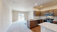 This single-story apartment at Hawk Ridge Trail in Lake Saint Louis, Missouri, offers a well-designed two-bedroom, one-bathroom layout with a neutral color palette and consistent finishes throughout. The open-concept kitchen and living area serves as the heart of the unit, where rich, dark-stained cabinetry pairs with light granite countertops and a full suite of stainless steel appliances, including a refrigerator, range, microwave, and dishwasher. A peninsula counter provides additional prep space and a natural transition into the carpeted living area, which receives natural light through a sliding glass door leading to a private balcony with exterior views. Both bedrooms are generously proportioned, carpeted, and finished with the same warm neutral tones; one bedroom also includes sliding glass door access to an outdoor balcony. The shared bathroom features matching dark cabinetry, granite countertops, hardwood-style flooring, and a tub-shower combination. A dedicated laundry area with a washer and shelving above adds everyday convenience. Hardwood-style flooring runs through the kitchen and bathroom, while plush carpet covers the living and bedroom areas, creating a comfortable and cohesive living environment.