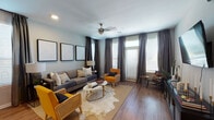 This well-designed single-floor residence offers a cohesive blend of modern aesthetics and functional living. The open-concept living area is a welcoming space anchored by rich hardwood-style flooring, a ceiling fan, and an abundance of natural light streaming through multiple large windows dressed with elegant floor-to-ceiling drapes. A gallery wall of framed artwork adds a curated touch, while the layout comfortably accommodates a generous seating arrangement centered around a cowhide area rug.

The kitchen flows seamlessly from the living space and features dark shaker-style cabinetry, granite countertops, a tile backsplash, and a full suite of stainless steel appliances. A spacious island with pendant lighting above doubles as a breakfast bar with seating, making it ideal for both cooking and casual dining.

The bedroom is a serene retreat highlighted by plush carpeting, a dramatic tall upholstered headboard, flanking nightstands, and a ceiling fan. Natural light filters in through a window with tailored drapes, creating a calm and restful atmosphere.

The bathroom is clean and efficiently laid out, with dark wood cabinetry, a single vanity with a large mirror, bright vanity lighting, and hardwood-style flooring that ties the space together with the rest of the home.