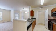 Located at 2000 Crossroads Manor Ct in Cary, NC, this single-floor residence offers a well-organized, open layout designed for comfortable everyday living. The kitchen serves as a central hub, featuring warm medium-toned wood cabinetry with dark countertops, stainless steel appliances including a refrigerator, range, and built-in microwave, a double-basin stainless steel sink, and a dishwasher. Light tile flooring runs throughout the kitchen, providing a clean, easy-to-maintain surface. A peninsula with a white countertop connects the kitchen to the adjoining living and dining area, creating a seamless open-concept flow. The living and dining space is generously proportioned, finished with plush carpeting, crown molding, and a pendant light fixture. Multiple windows dressed with blinds invite an abundance of natural light, while a glass-paned exterior door provides direct outdoor access. The bedroom is a quiet, comfortable retreat with soft carpeting underfoot and a window overlooking the surrounding neighborhood. The bathroom includes a full soaking tub with white tile surround, offering a clean and classic finish. Throughout the residence, neutral warm-beige walls and white trim create a cohesive, inviting atmosphere.