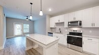 Located at Annapolis Loop in Ellenton, Florida, this well-appointed one-bedroom, one-bathroom residence offers a thoughtfully designed single-floor layout. The open-concept kitchen and living area serves as the heart of the home, showcasing crisp white shaker cabinetry, granite countertops, and a central kitchen island illuminated by sleek pendant lighting. A full suite of stainless steel appliances — including a refrigerator with ice maker, electric range, microwave, and dishwasher — completes the kitchen. Light wood-look flooring runs throughout the main living areas, lending warmth and continuity to the space. The living room receives natural light through a glass door leading to an outdoor area, and a ceiling fan adds comfort. The bedroom is a comfortable, well-proportioned retreat featuring plush carpeting, dual windows with exterior views, and a ceiling fan. A dedicated closet provides organized storage. The bathroom offers a tub-shower combination with vertically tiled surround and wood-look tile flooring, accented by matte black hardware. A separate laundry room houses a full-size Whirlpool washer and dryer with overhead wire shelving. The overall aesthetic is clean, modern, and move-in ready.