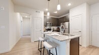This well-appointed single-floor residence showcases a thoughtful layout and contemporary finishes throughout. The kitchen serves as a central highlight, featuring dark wood cabinetry, granite countertops, a white subway tile backsplash, and a full suite of stainless steel appliances including a refrigerator, electric range, and over-the-range microwave. A peninsula island with seating for two is illuminated by sleek pendant lighting, making it an ideal space for casual dining and entertaining.

The living area is bright and open, with light wood-style flooring, a ceiling fan, and a sliding glass door with vertical blinds that invite natural light into the space. The bedrooms are carpeted for comfort, each featuring ceiling fans and generous proportions. At least one bedroom includes access to a walk-in closet with built-in shelving, offering substantial storage capacity.

Both bathrooms are finished consistently with the rest of the home, featuring granite-topped dark wood vanities, light wood-style flooring, and full soaking tub and shower combinations with clean white tile surrounds. The overall aesthetic is modern and neutral, with a cohesive palette of whites, warm grays, and natural wood tones creating a welcoming and functional living environment.