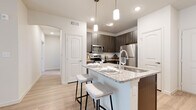 This well-appointed single-floor residence showcases a thoughtful layout and contemporary finishes throughout. The kitchen serves as a central highlight, featuring dark wood cabinetry, granite countertops, a white subway tile backsplash, and a full suite of stainless steel appliances including a refrigerator, electric range, and over-the-range microwave. A peninsula island with seating for two is illuminated by sleek pendant lighting, making it an ideal space for casual dining and entertaining.

The living area is bright and open, with light wood-style flooring, a ceiling fan, and a sliding glass door with vertical blinds that invite natural light into the space. The bedrooms are carpeted for comfort, each featuring ceiling fans and generous proportions. At least one bedroom includes access to a walk-in closet with built-in shelving, offering substantial storage capacity.

Both bathrooms are finished consistently with the rest of the home, featuring granite-topped dark wood vanities, light wood-style flooring, and full soaking tub and shower combinations with clean white tile surrounds. The overall aesthetic is modern and neutral, with a cohesive palette of whites, warm grays, and natural wood tones creating a welcoming and functional living environment.