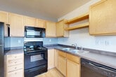 Located at 301 Second St E in Williston, North Dakota, this single-floor unit offers a practical and efficiently designed layout. The combined kitchen and living area serves as the heart of the space, featuring light wood-tone flooring that extends throughout, creating a bright and cohesive feel. The kitchen is well-equipped with light maple cabinetry, dark countertops, and a full suite of black appliances including a refrigerator, electric range, over-the-range microwave, and dishwasher. Ample upper and lower cabinet storage ensures functional use of the kitchen space. Natural light flows into the living area through windows fitted with blinds, offering views of the surrounding neighborhood and keeping the space feeling open and airy. The clean white walls throughout the unit provide a neutral backdrop that complements the light flooring. Baseboard heating is present along the living area walls, providing efficient warmth during North Dakota winters. A dedicated laundry area accommodates a stacked Whirlpool washer and dryer unit on tile flooring, adding a convenient in-unit amenity. Overall, the space presents a clean, functional layout well-suited for everyday living.