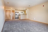 This single-floor residence offers a thoughtfully designed open-concept layout that seamlessly connects the kitchen and living areas. The kitchen is equipped with stainless steel appliances, including a side-by-side refrigerator with an ice and water dispenser and a stainless range, complemented by white cabinetry, dark countertops, recessed lighting, and tile flooring. A peninsula with a granite-style countertop and an integrated sink serves as both a functional workspace and a natural divider between the kitchen and the expansive carpeted living area. The living space is bright and open, with access to a private balcony that allows natural light to filter in through sliding glass doors. The bedrooms are generously sized, each featuring plush carpeting, wood-trimmed windows that bring in ample daylight, and neutral walls. The primary bedroom benefits from a large walk-in closet outfitted with wire shelving and hanging rods. The bathroom includes a wide vanity with an undermount sink and a full-width mirror. A dedicated in-unit laundry closet houses a full-size washer and dryer. Throughout the space, warm wood-toned doors and trim provide a cohesive, classic aesthetic against the neutral color palette.