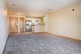 This single-floor residence offers a thoughtfully designed open-concept layout that seamlessly connects the kitchen and living areas. The kitchen is equipped with stainless steel appliances, including a side-by-side refrigerator with an ice and water dispenser and a stainless range, complemented by white cabinetry, dark countertops, recessed lighting, and tile flooring. A peninsula with a granite-style countertop and an integrated sink serves as both a functional workspace and a natural divider between the kitchen and the expansive carpeted living area. The living space is bright and open, with access to a private balcony that allows natural light to filter in through sliding glass doors. The bedrooms are generously sized, each featuring plush carpeting, wood-trimmed windows that bring in ample daylight, and neutral walls. The primary bedroom benefits from a large walk-in closet outfitted with wire shelving and hanging rods. The bathroom includes a wide vanity with an undermount sink and a full-width mirror. A dedicated in-unit laundry closet houses a full-size washer and dryer. Throughout the space, warm wood-toned doors and trim provide a cohesive, classic aesthetic against the neutral color palette.