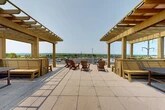 Located at 16 Cinema Dr in Lansing, NY, this rooftop terrace offers an expansive outdoor retreat designed for relaxation and social gathering. The space is defined by its open, tiled terrace deck, bordered by sleek horizontal metal railings that provide unobstructed panoramic views of the rolling hills, lush greenery, and open skies characteristic of the Finger Lakes region.

Two substantial wood-framed pergolas anchor opposite sides of the terrace, providing partial shade while preserving the airy, open-air atmosphere. Beneath each pergola, built-in wooden bench seating and picnic-style tables create comfortable gathering nooks ideal for conversation or al fresco dining. Raised wooden planter boxes line the perimeter, adding greenery and a warm, natural aesthetic to the space.

At the center of the terrace, a cluster of classic Adirondack chairs invites visitors to sit back and take in the sweeping views. The large-format tile flooring ties the entire space together, lending a clean, modern finish to the rooftop. The overall ambiance is bright, welcoming, and open, making this terrace a standout communal amenity suited for enjoying warm-weather days and the scenic natural surroundings of Lansing, New York.