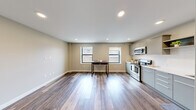 Located at 201 Michigan St NW in the heart of Grand Rapids, Michigan, this efficiently designed single-floor unit offers a thoughtful layout that maximizes every square foot. The open living area is finished with warm hardwood-style flooring throughout, recessed lighting, and neutral-toned walls that create a clean, modern atmosphere. Two windows along the main living space allow natural light to filter in, enhancing the bright and airy feel of the interior.

The contemporary kitchen is well-appointed with flat-front grey cabinetry, white quartz countertops, a subway tile backsplash, open upper shelving, and stainless steel appliances including a refrigerator, electric range with microwave hood, and dishwasher. A long hallway connects the living and sleeping areas, flanked by built-in storage panels that make excellent use of the corridor space. A standout architectural detail is the sleek frosted glass sliding barn door, which separates the bedroom from the rest of the unit, adding a modern, upscale touch while maintaining an open feel. The bedroom also features dark-toned wardrobe cabinetry. The unit includes integrated speakers, ventilation, and recessed lighting throughout, reflecting a well-considered, modern design approach.