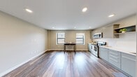 Located at 201 Michigan St NW in the heart of Grand Rapids, Michigan, this efficiently designed single-floor unit offers a thoughtful layout that maximizes every square foot. The open living area is finished with warm hardwood-style flooring throughout, recessed lighting, and neutral-toned walls that create a clean, modern atmosphere. Two windows along the main living space allow natural light to filter in, enhancing the bright and airy feel of the interior.

The contemporary kitchen is well-appointed with flat-front grey cabinetry, white quartz countertops, a subway tile backsplash, open upper shelving, and stainless steel appliances including a refrigerator, electric range with microwave hood, and dishwasher. A long hallway connects the living and sleeping areas, flanked by built-in storage panels that make excellent use of the corridor space. A standout architectural detail is the sleek frosted glass sliding barn door, which separates the bedroom from the rest of the unit, adding a modern, upscale touch while maintaining an open feel. The bedroom also features dark-toned wardrobe cabinetry. The unit includes integrated speakers, ventilation, and recessed lighting throughout, reflecting a well-considered, modern design approach.