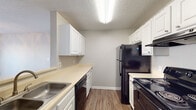 This single-floor space offers a functional and straightforward layout designed to maximize efficiency. Wood-look flooring runs consistently throughout the unit, providing a cohesive look and easy maintenance. Neutral gray and beige tones on the walls create a clean, understated backdrop across all rooms.

The galley-style kitchen is well-equipped, featuring white cabinetry with ample upper and lower storage, light-toned countertops, a stainless steel sink, and black appliances including a refrigerator, electric range, and dishwasher. A pass-through counter opening connects the kitchen to the adjacent living area, adding a sense of openness between the two spaces.

The living area is open and versatile, with a front entry door and direct sightlines into the kitchen pass-through. A ceiling fan with light fixture is present in the bedroom, which benefits from a window that brings in natural light and an outdoor view. A closet with louvered bifold doors provides storage within the bedroom, and an additional closet is accessible in the hallway area.

The bathroom includes a single-sink vanity with white cabinetry and a speckled countertop, a full tub-shower combination, and a textured ceiling consistent with the rest of the unit. Textured ceilings are featured throughout, adding a classic residential character to the space.