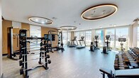 Located at 200 Daytona Blvd in Daytona Beach, FL, this contemporary fitness center is a well-appointed, single-floor facility offering a comprehensive workout environment. The space is divided into two distinct zones designed to accommodate a full range of exercise needs.

The main strength and cardio area features an impressive array of equipment, including treadmills, ellipticals, stationary bikes, a Smith machine, and a full rack of dumbbells. A large flat-screen television is mounted on the wall, and floor-to-ceiling windows line the perimeter, flooding the space with natural light and offering views of the surrounding Daytona Beach landscape, including palm trees and the colorful cityscape beyond.

A secondary functional training area provides an open, flexible floor plan ideal for dynamic workouts. This zone is equipped with medicine balls, kettlebells, and plyometric boxes, and benefits from the same expansive window views and abundant natural light. Large sliding glass doors lead directly outside, enhancing the airy atmosphere.

Throughout the facility, the design aesthetic is sleek and modern, defined by warm wood slat accent walls, full-length mirrors, durable wood-tone flooring, and signature oval-shaped recessed lighting fixtures that lend the space a sophisticated, boutique-gym ambiance.