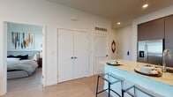 This single-floor residence is thoughtfully designed with a modern aesthetic, offering a seamless flow between its primary living spaces. The open-concept kitchen serves as a central hub, outfitted with two-tone cabinetry featuring white upper cabinets and dark lower cabinets, stone countertops, a classic white subway tile backsplash, and stainless steel appliances including a gas range and French door refrigerator. A peninsular island with stone countertops provides seating for multiple bar stools, making it ideal for casual dining and entertaining.

The living area is bright and welcoming, benefiting from natural light through large windows with views to the outdoors. Light wood-tone flooring runs consistently throughout the unit, contributing to a cohesive, airy feel. The space is versatile enough to accommodate both a lounge setup and a dedicated workspace.

Two bedrooms offer comfortable accommodations, each with windows that admit natural light. The bathroom features a stone-topped vanity with white cabinetry, a large mirror, and light wood flooring. Additional storage is provided by a double-door closet in the entry area. Recessed lighting and clean white walls complete the contemporary character of this well-appointed residence.
