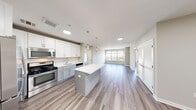 Located at 303 Main St in Hempstead, NY, this well-appointed 2-bedroom, 2-bathroom residence offers a thoughtfully designed single-floor layout with a clean, contemporary aesthetic. Light-toned wood-style flooring runs throughout the entire space, creating a cohesive and modern feel.

The open-concept kitchen and living area forms the heart of the home. The kitchen features crisp white upper cabinetry, gray lower cabinetry, light quartz countertops, stainless steel appliances including a gas range, microwave, refrigerator, and dishwasher, and a center island providing additional prep and seating space. Pendant lighting above the island adds a stylish touch, while recessed lighting ensures the area remains bright. The kitchen flows seamlessly into the spacious living area, which benefits from large windows that bring in generous natural light and offer views of the surrounding neighborhood.

Both bedrooms are well-sized, with the primary bedroom featuring a walk-in closet equipped with wire shelving for organized storage, as well as a dedicated window. The second bedroom also includes a window with outdoor views. A connecting hallway provides access to both bathrooms, one of which features a white vanity, tiled tub-shower combination with chrome grab bars, and wood-style flooring. The layout is completed by two closets and a functional hallway entry.