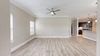 This single-story, 3-bedroom, 2-bathroom home is thoughtfully designed with a cohesive neutral palette and consistent light-toned wood-look flooring that flows throughout every room. Crown molding and ceiling fans with integrated lighting are featured in the living areas and bedrooms, adding a polished, finished look to the space.

The living room is generously sized, bathed in natural light from blinded windows, and accented with clean white baseboards against warm beige walls. The kitchen features dark espresso cabinetry, granite countertops, a subway tile backsplash, and stainless steel appliances, including a range, microwave, and refrigerator, with direct access to an exterior door.

The spacious primary bedroom accommodates large furniture comfortably and includes a walk-in closet outfitted with wire shelving on multiple walls for ample storage. The two bathrooms are finished with granite-topped dark vanities and wood-look tile flooring; one features a walk-in glass-door shower. Two additional bedrooms offer natural light through windows with blinds and ceiling fans overhead.

A dedicated laundry room houses a full-size washer and dryer. Hallways connect the rooms efficiently, completing this well-organized and move-in-ready home.