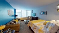 Located at 2851 S Dr Martin Luther King Jr Dr in Chicago's Bronzeville neighborhood, this single-floor unit offers a well-organized layout incorporating a living area, sleeping quarters, kitchen, and full bathroom. The living area serves as an eye-catching focal point, featuring a bold blue accent wall, carpet flooring, and a large bank of windows fitted with horizontal blinds that allow generous natural light to fill the space. A wall-mounted air conditioning unit provides climate control beneath the expansive window.

The sleeping area connects seamlessly to the living space, demonstrating the unit's open-concept character. It features neutral carpet, a softly lit accent wall, and ample room for bedroom furnishings including a full dresser. A mirrored sliding closet door is visible, adding practical storage.

The kitchen is efficiently designed with white cabinetry, dark countertops, tile flooring, a gas range, and a full-size refrigerator. Compact yet functional, it provides all essential cooking amenities. The bathroom is clean and straightforward, featuring a tub/shower combination, a mirrored medicine cabinet, and a white vanity with under-sink storage. Overall, the unit presents a practical, light-filled living environment well-suited to urban Chicago living.