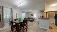 This single-floor residence offers a cohesive and functional layout that flows naturally from one area to the next. The open-concept living and dining space is anchored by light hardwood-style flooring and elegant crown molding that frames the ceilings throughout. The living area provides a comfortable and relaxed atmosphere, featuring large windows dressed with blinds and curtains that allow ample natural light to fill the room. The dining area is positioned adjacent to the living space, illuminated by a modern multi-light track fixture overhead, making it ideal for everyday meals or hosting guests. The galley-style kitchen is efficiently designed with light wood cabinetry, granite-look countertops, a double basin sink, and a full suite of black and stainless steel appliances including a range, refrigerator, microwave, and dishwasher. A raised breakfast bar separates the kitchen from the main living area, adding both functionality and an open feel. The bedroom offers a serene retreat with plush carpet flooring, a ceiling fan with light, and a window that brings in soft natural light. The full bathroom includes a wide vanity with ample cabinet storage, a large mirror, and a tub-shower combination, all finished in a clean, neutral palette.