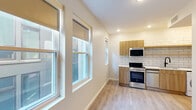 This efficiently designed single-floor studio makes smart use of its intimate footprint, delivering a modern and well-appointed living experience. The open layout flows naturally from the sleeping area to the kitchen, unified by light wood-tone laminate flooring throughout.

The kitchen is a standout feature, outfitted with warm wood cabinetry, a classic white subway tile backsplash, and quartz countertops. Stainless steel appliances — including a range, dishwasher, microwave, and refrigerator — are complemented by an in-unit washer, a single-basin sink with a matte black faucet, and open shelving for additional storage. Multiple windows invite generous natural light into the kitchen and main living area.

The sleeping area is a calm, neutral space with soft wall tones, a built-in double-door closet, and large windows with roller shades that frame views of the surrounding urban streetscape.

The bathroom is finished with floor-to-ceiling vertical white subway tiles and a dark mosaic marble shower floor, creating a striking contrast. A built-in shower niche adds a functional design touch, alongside a standard toilet and clean, minimal fixtures.

Recessed lighting throughout and a neutral color palette give the space a bright, contemporary feel well-suited for efficient urban living.